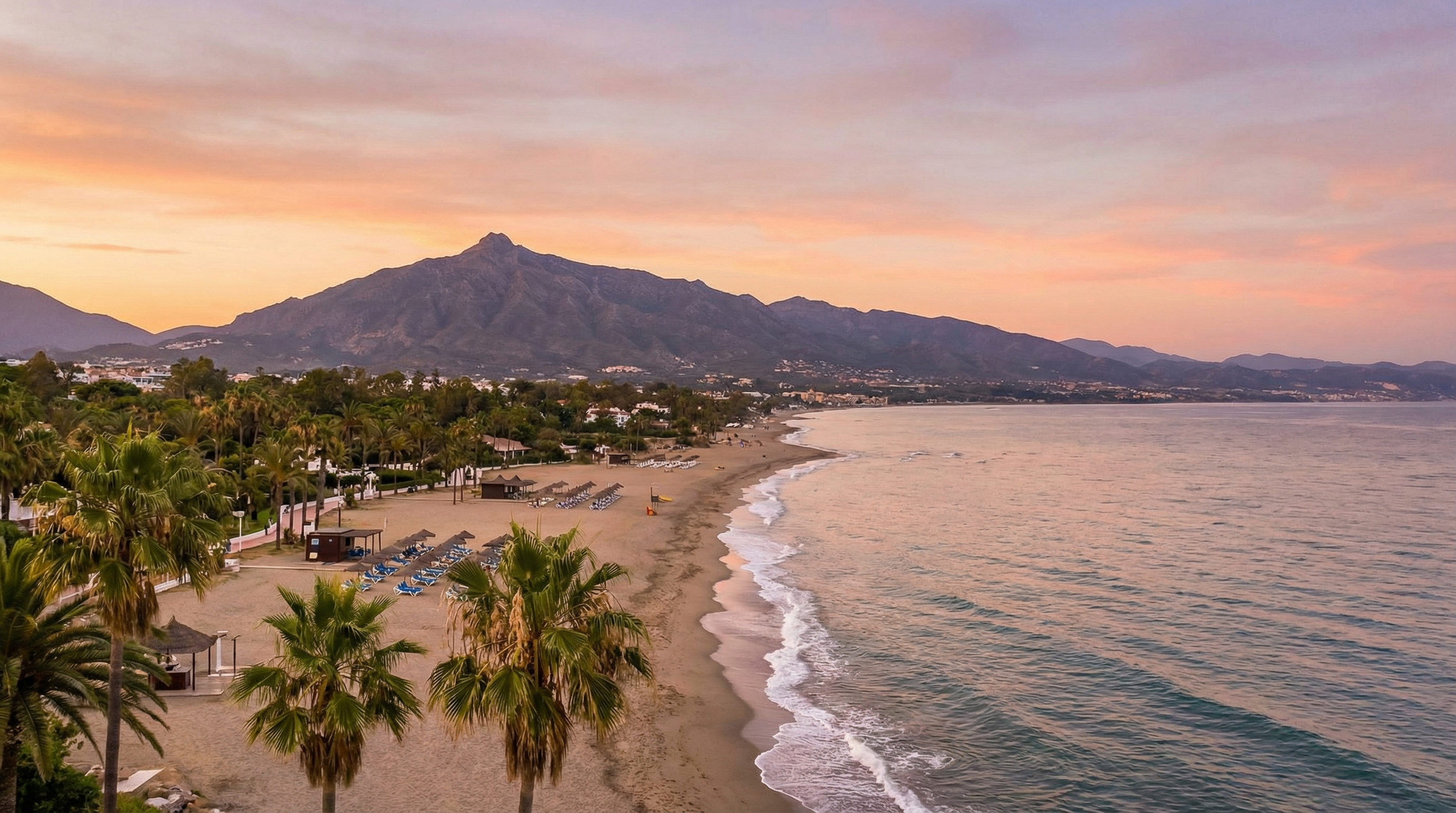 Panoramic view of Costa del Sol coastline at sunset, featuring golden beaches, Sierra Blanca mountains, and a serene beach scene with palm trees.