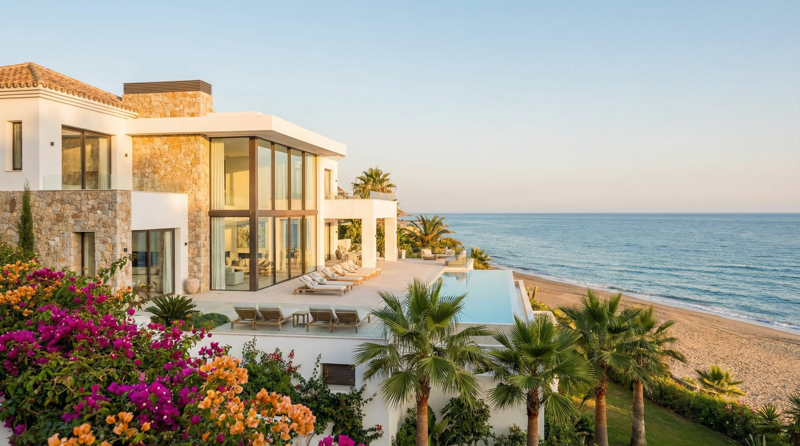 A modern beachfront property on the Costa del Sol with large glass windows, a spacious terrace, and vibrant bougainvillea, showcasing Mediterranean architecture.