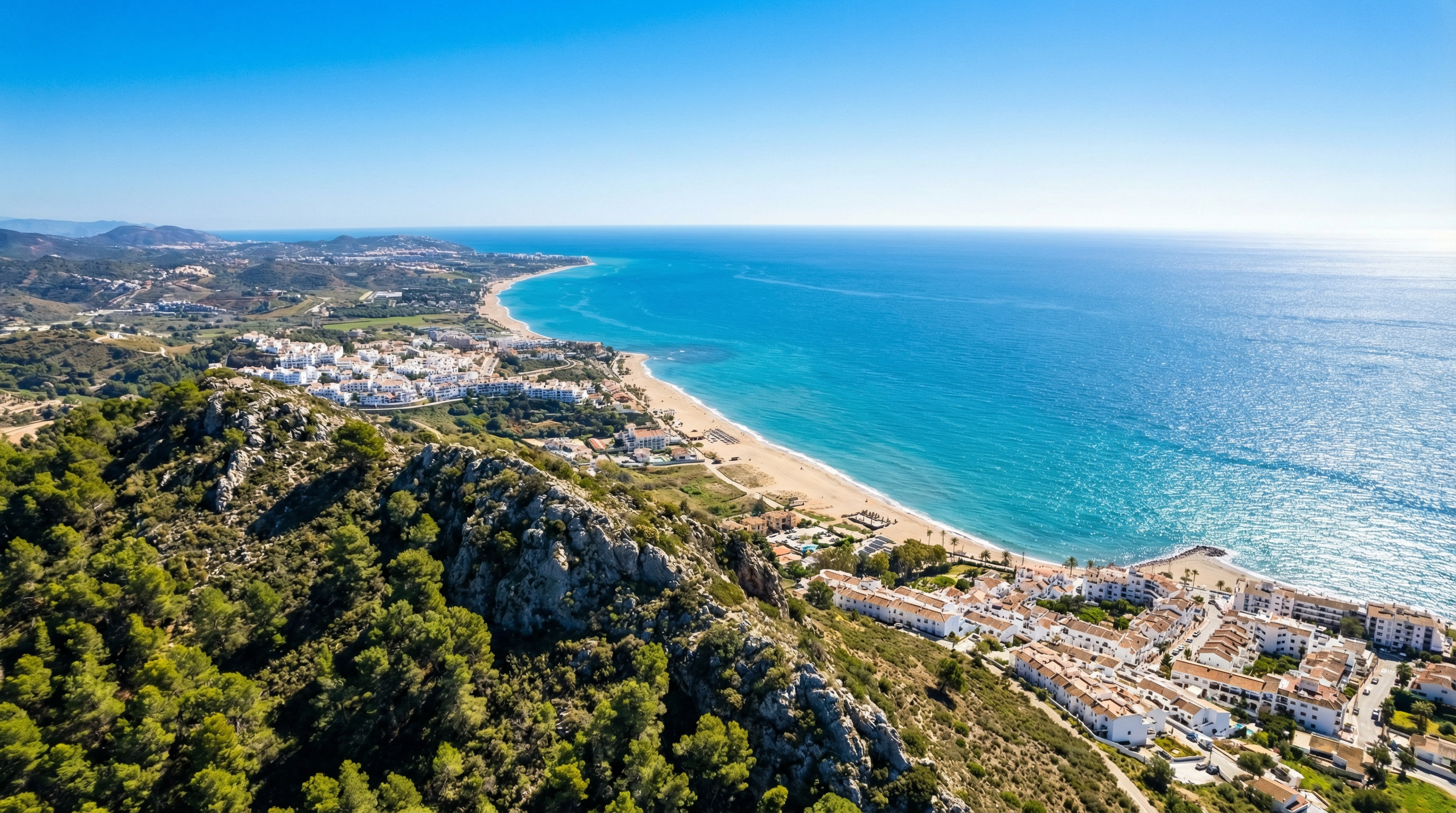 Aerial view of Costa del Sol coastline with vibrant Mediterranean waters, sandy beaches, and Sierra de Mijas mountains under a clear blue sky.