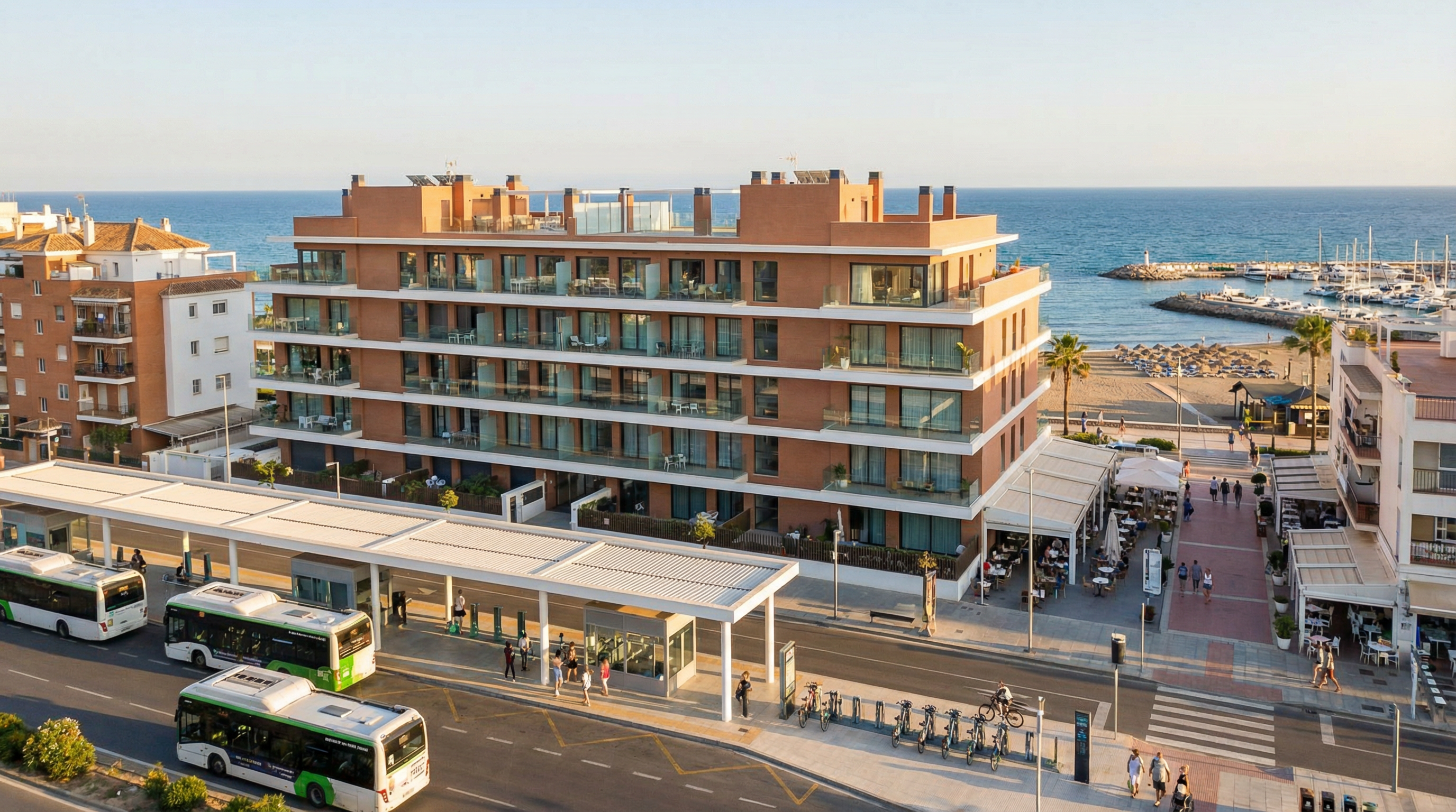 Panoramablick auf die Costa del Sol mit modernem Apartmentkomplex und öffentlicher Verkehrsanbindung. Bunte Promenade und lebhafte Strandatmosphäre sind sichtbar.