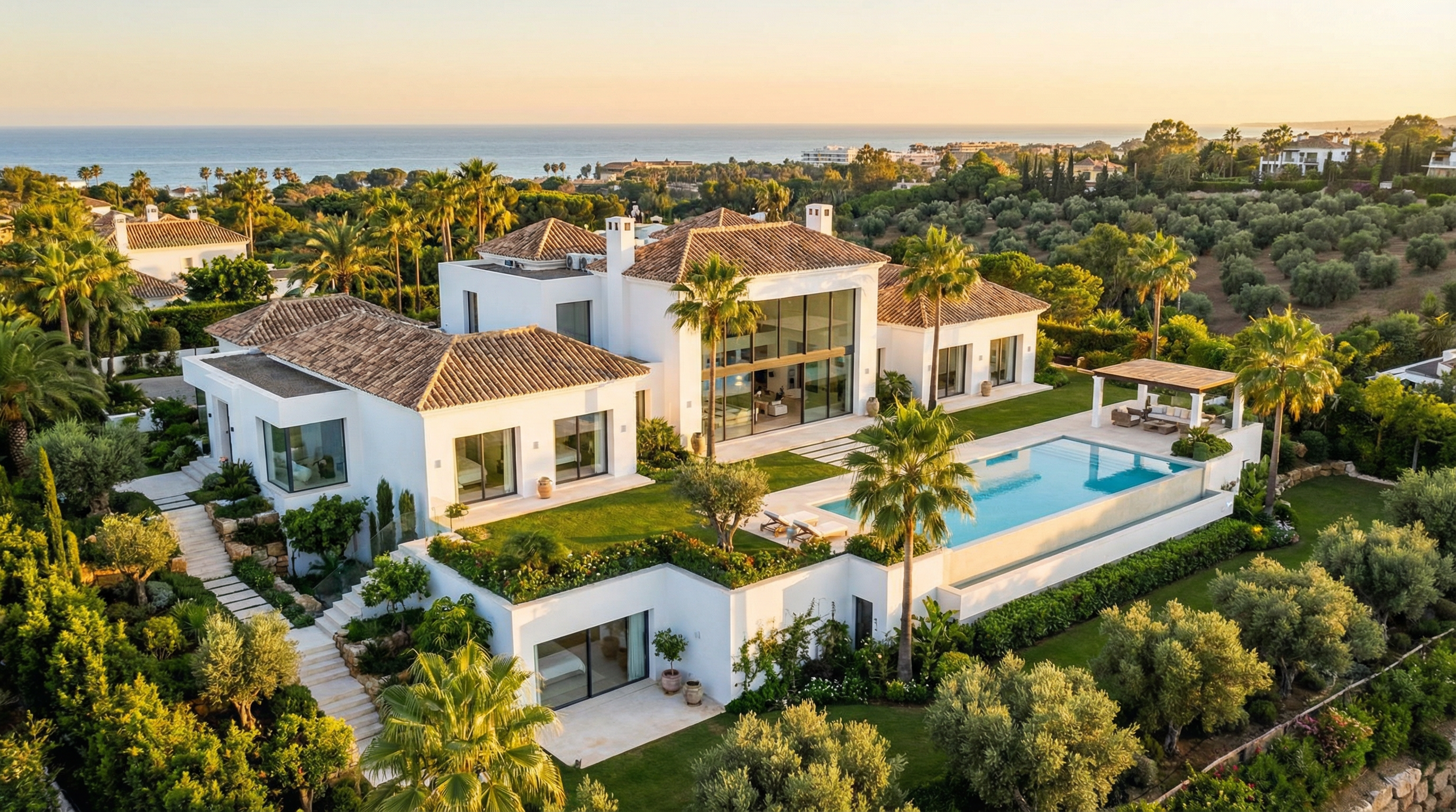 Luftaufnahme einer modernen Villa an der Costa del Sol mit weißen Wänden, Terrakottadächern und großen Fenstern, umgeben von Palmen und Gärten.